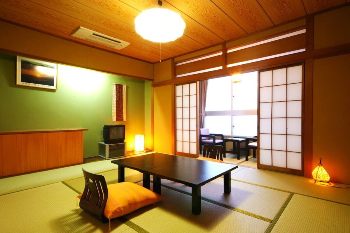 A traditional Japanese room with tatami flooring, a low table, a cushion, a television, and sliding doors.