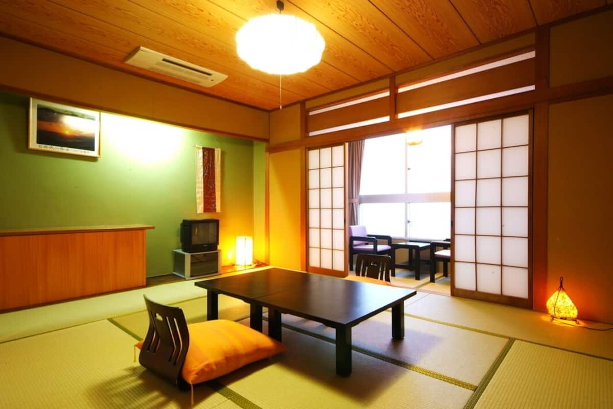 A traditional Japanese room with tatami flooring, a low table, a cushion, a television, and sliding doors.