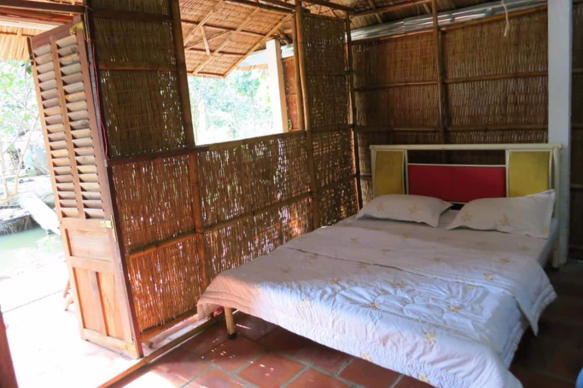 A room with a bed, a wooden door, and a thatched roof.