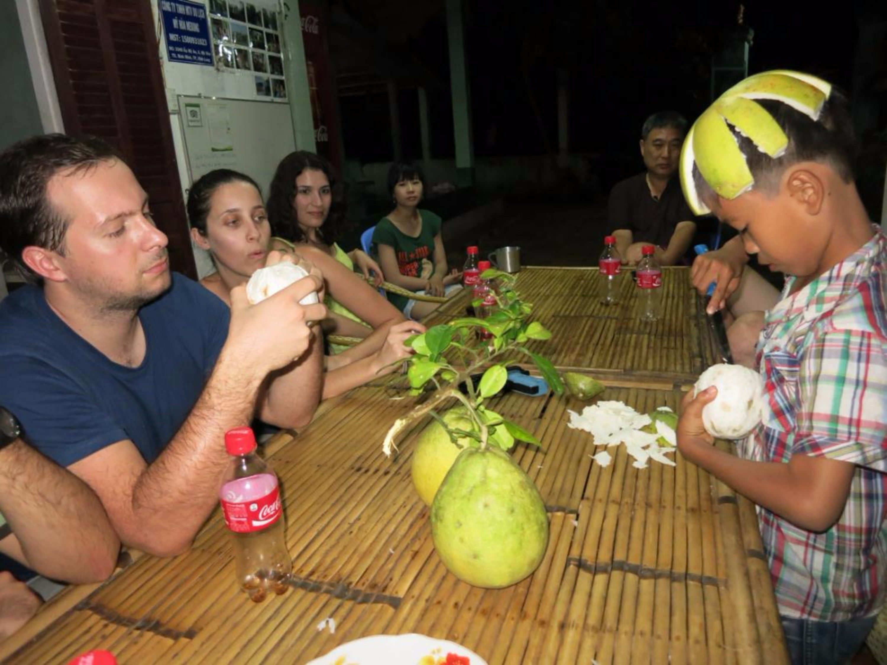 Um grupo de pessoas sentadas à mesa com uma goiaba grande e uma garrafa de Coca-Cola.