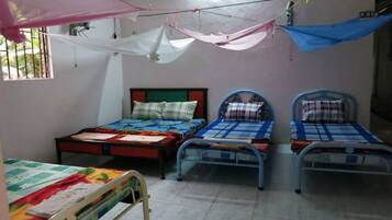 A room with three beds, each with a different headboard design. There is a window on the left side, and a mosquito net hanging above the beds.
