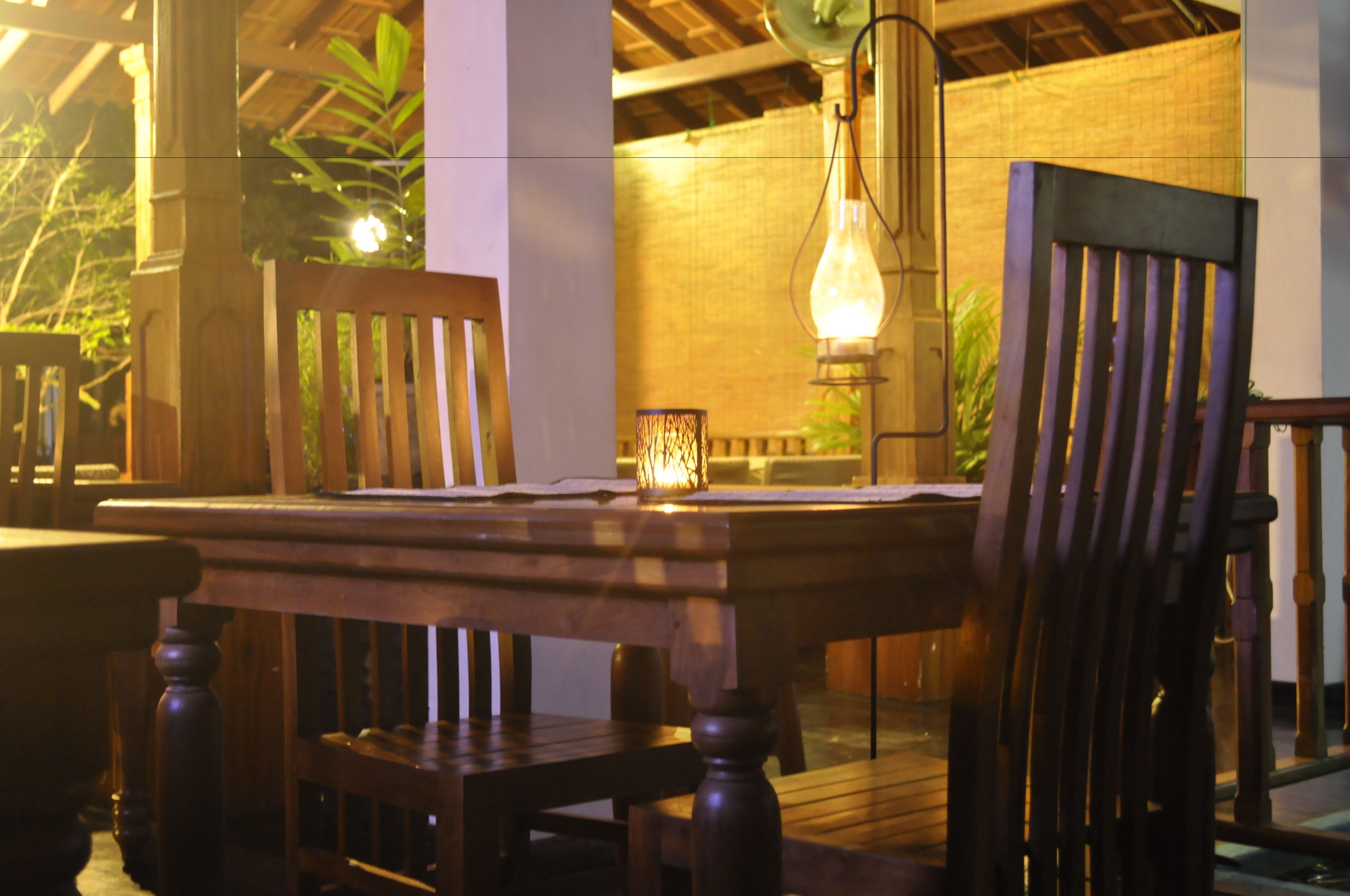 Una mesa de comedor de madera con sillas, una lámpara colgante y un muro de ladrillo al fondo.