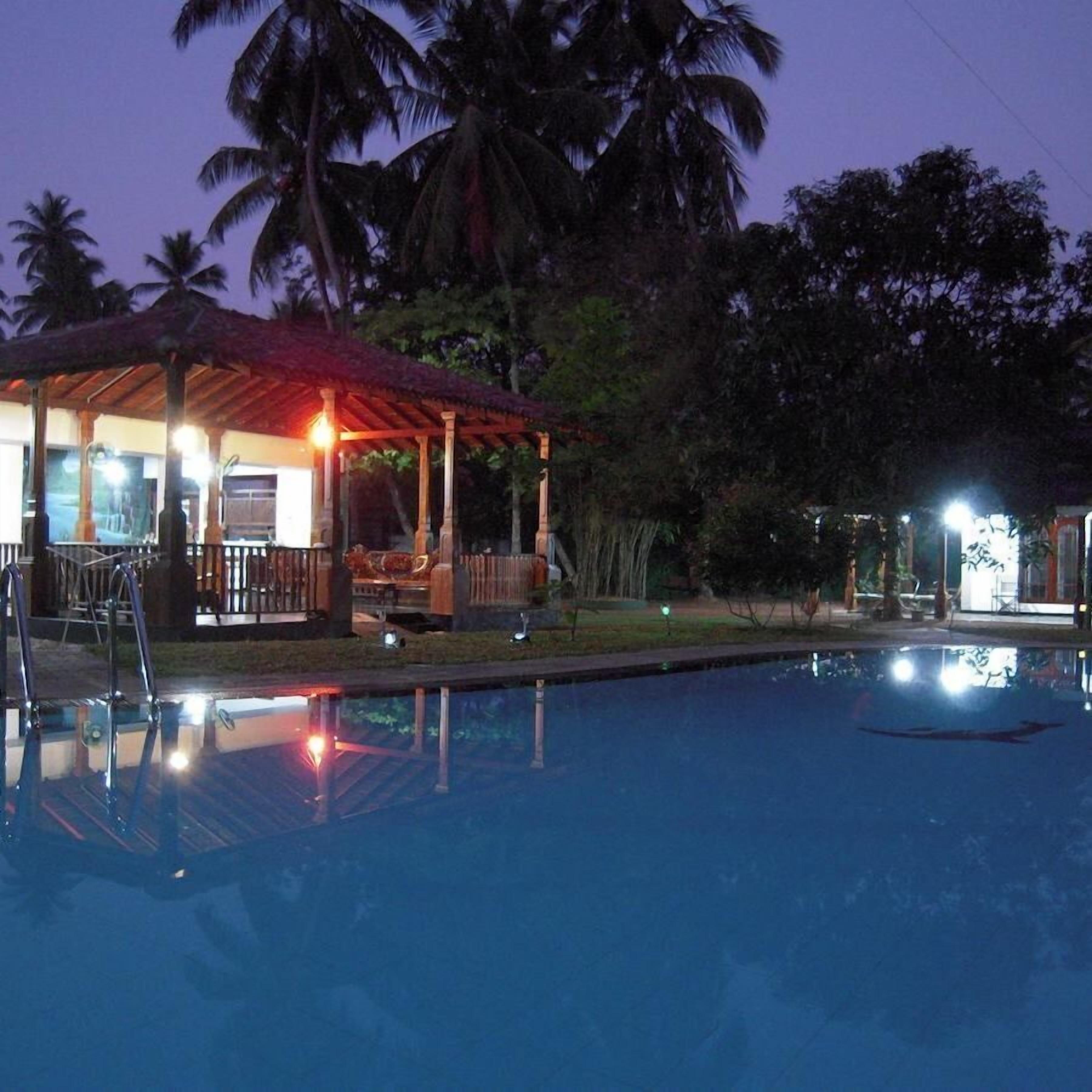 A pool area with a covered seating area and a building with a red roof.
