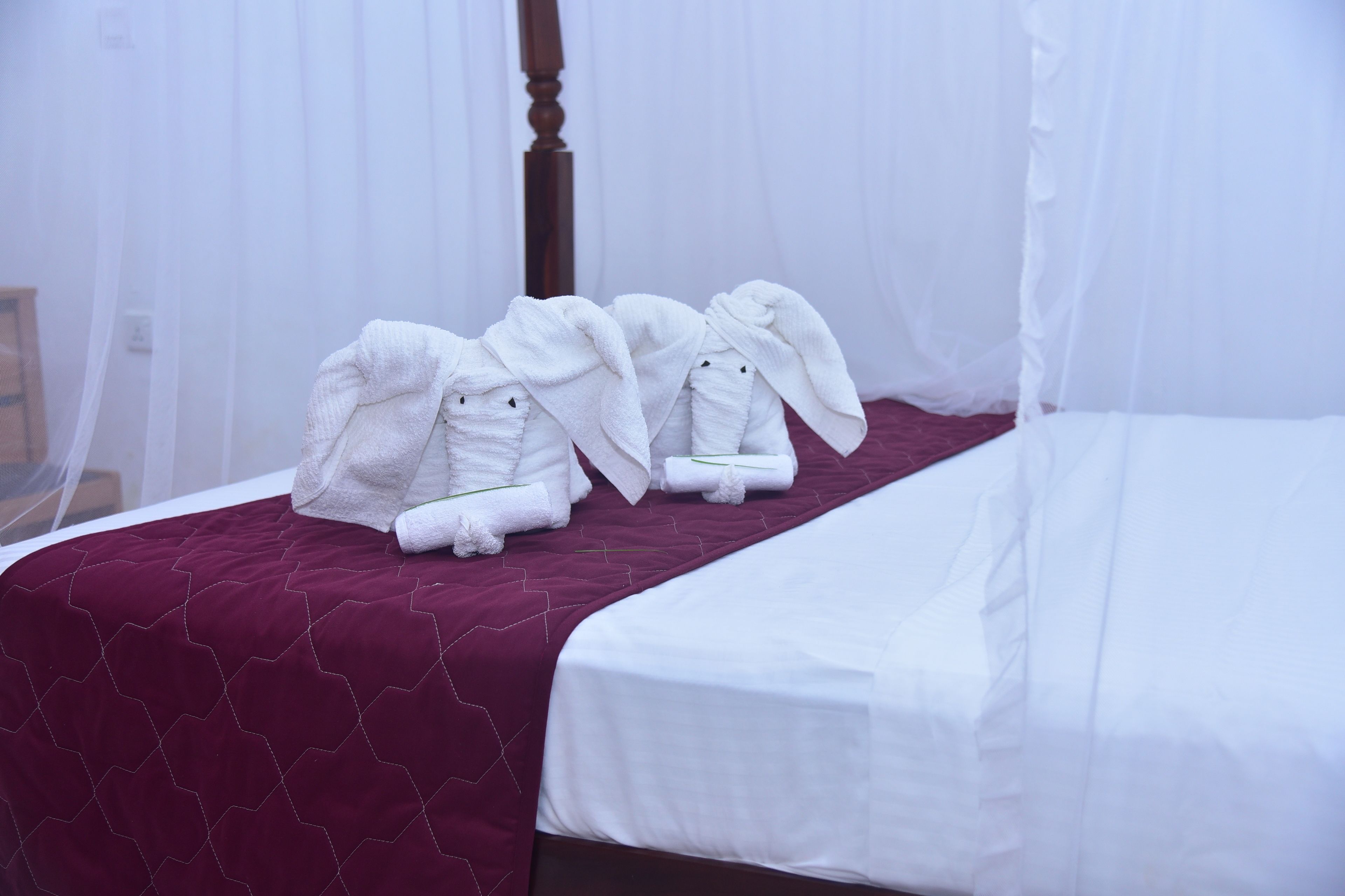 Habitación de hotel con una cama cubierta por una sábana blanca, un edredón rojo y dos toallas dobladas con cuidado sobre la cama.