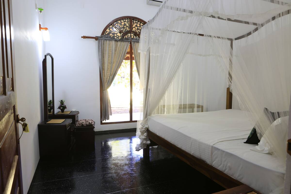 A bedroom with a bed, a nightstand, a mirror, and a window with curtains.