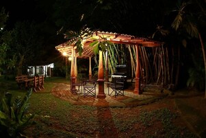 Un mirador con suelo de baldosas y mobiliario de madera, rodeado de palmeras y follaje.