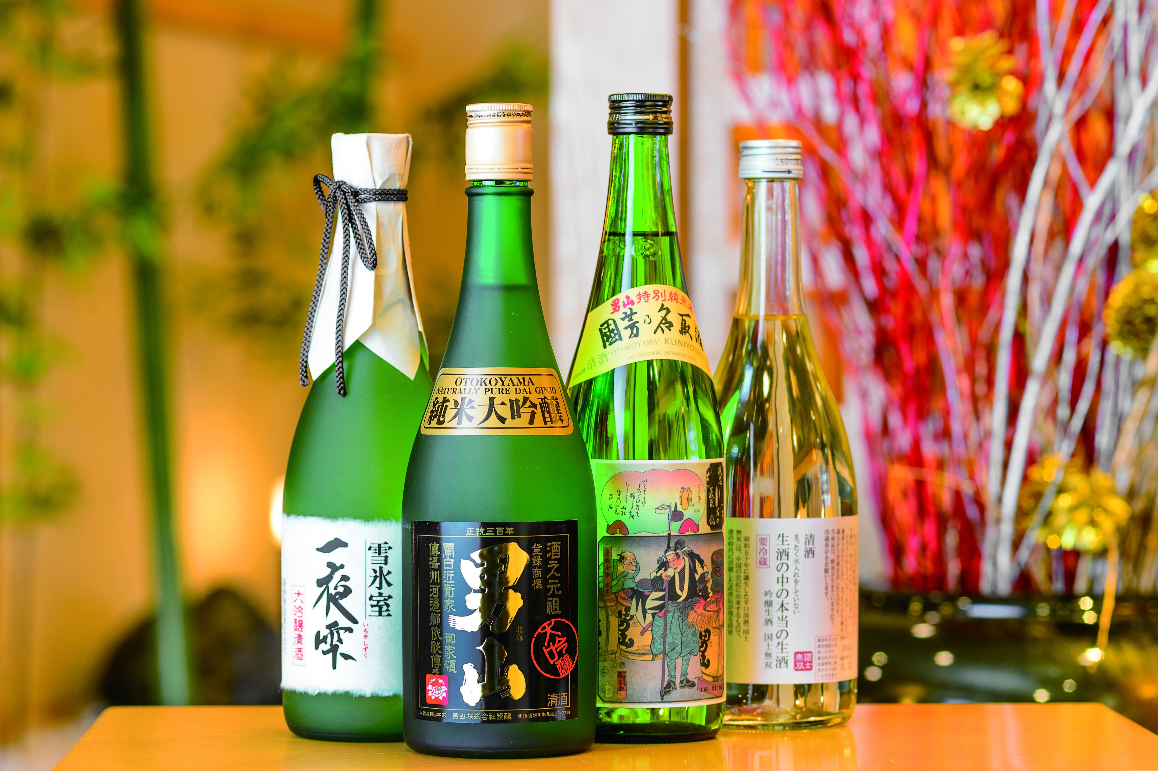 Cuatro botellas de sake sobre una mesa con fondo desenfocado.