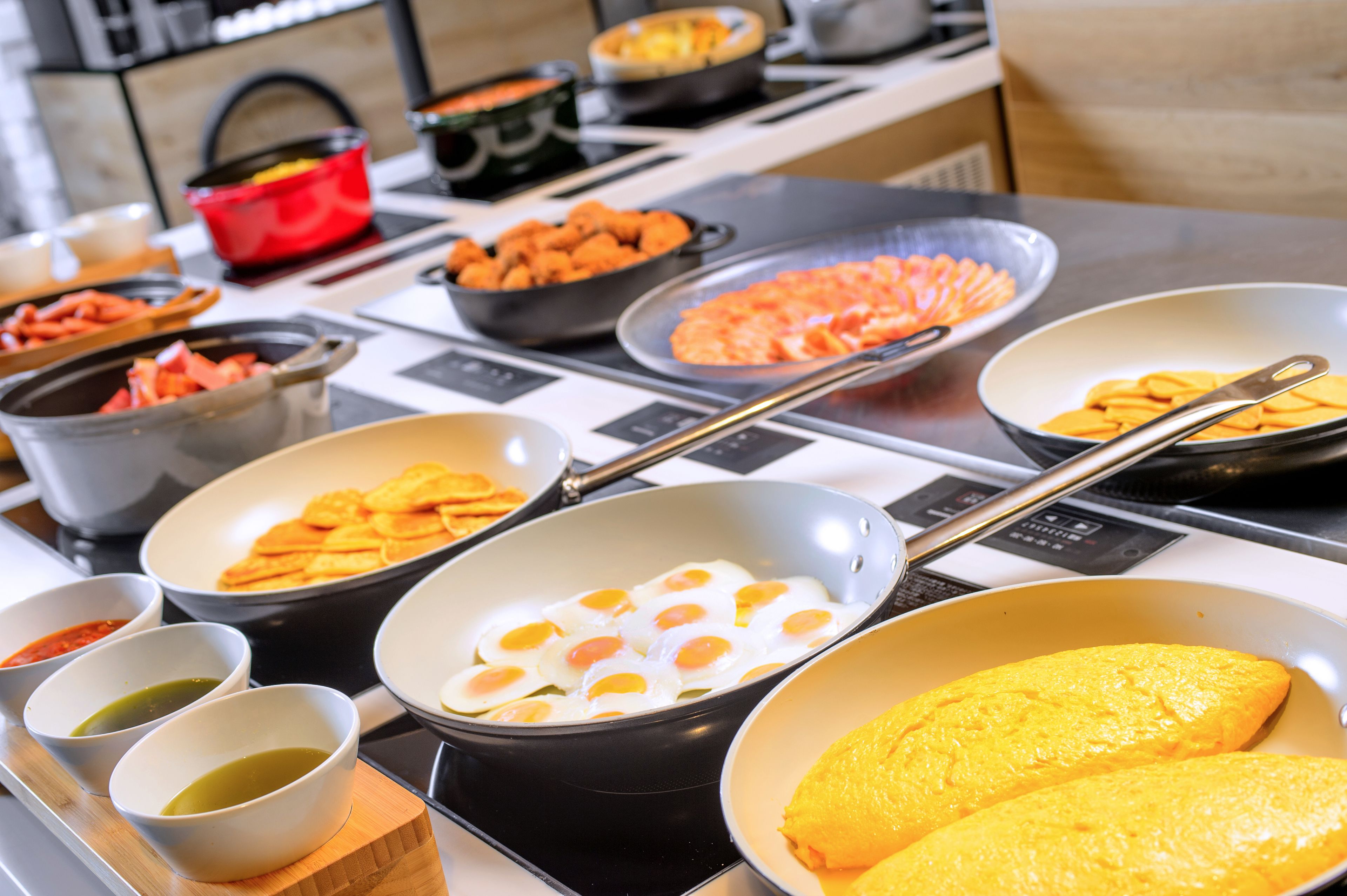 A kitchen with various cooking stations, including pans with eggs and vegetables, and bowls of sauces.