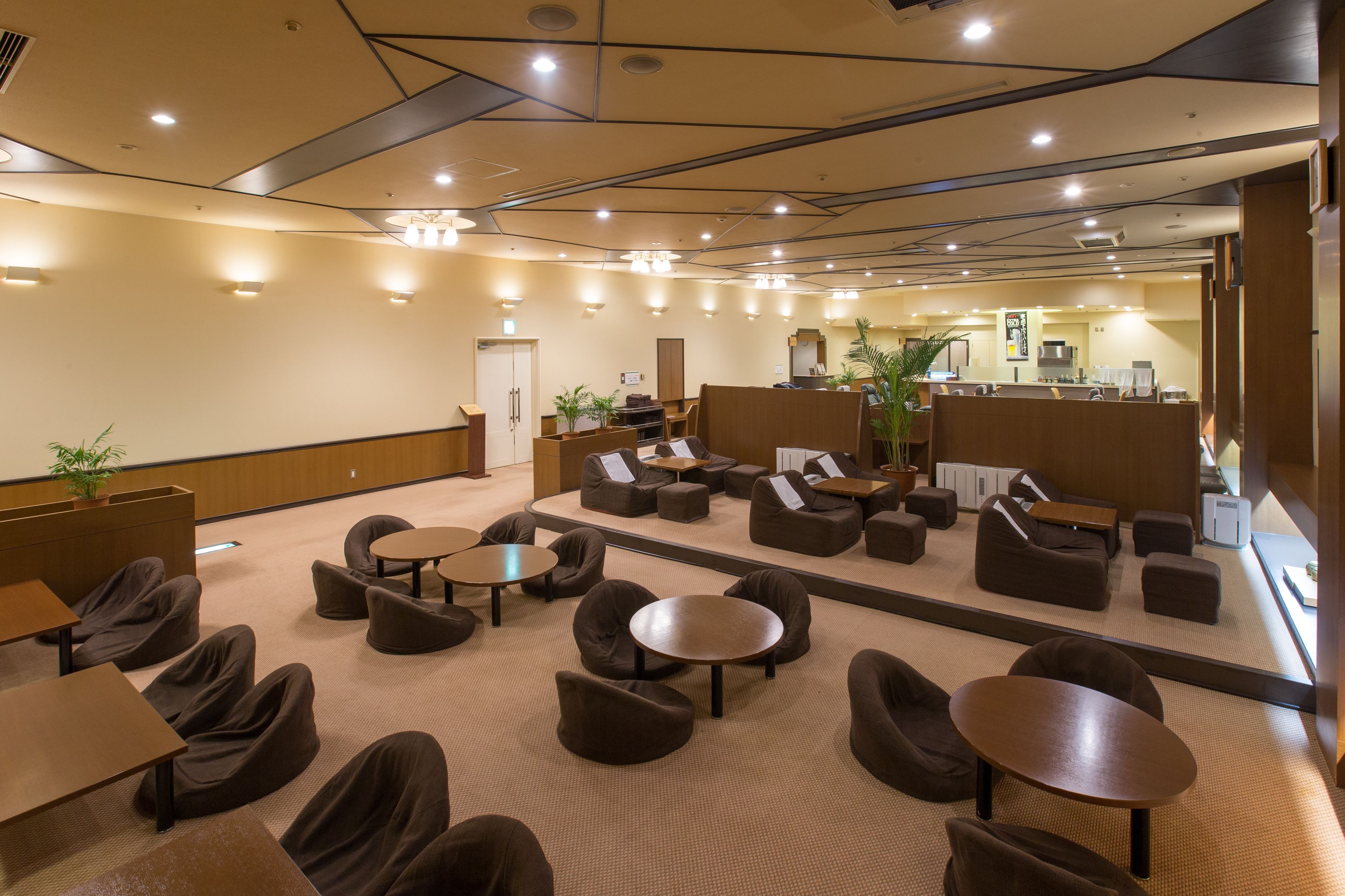 A modern lounge area with sofas and tables, a reception desk, and a kitchen in the background.