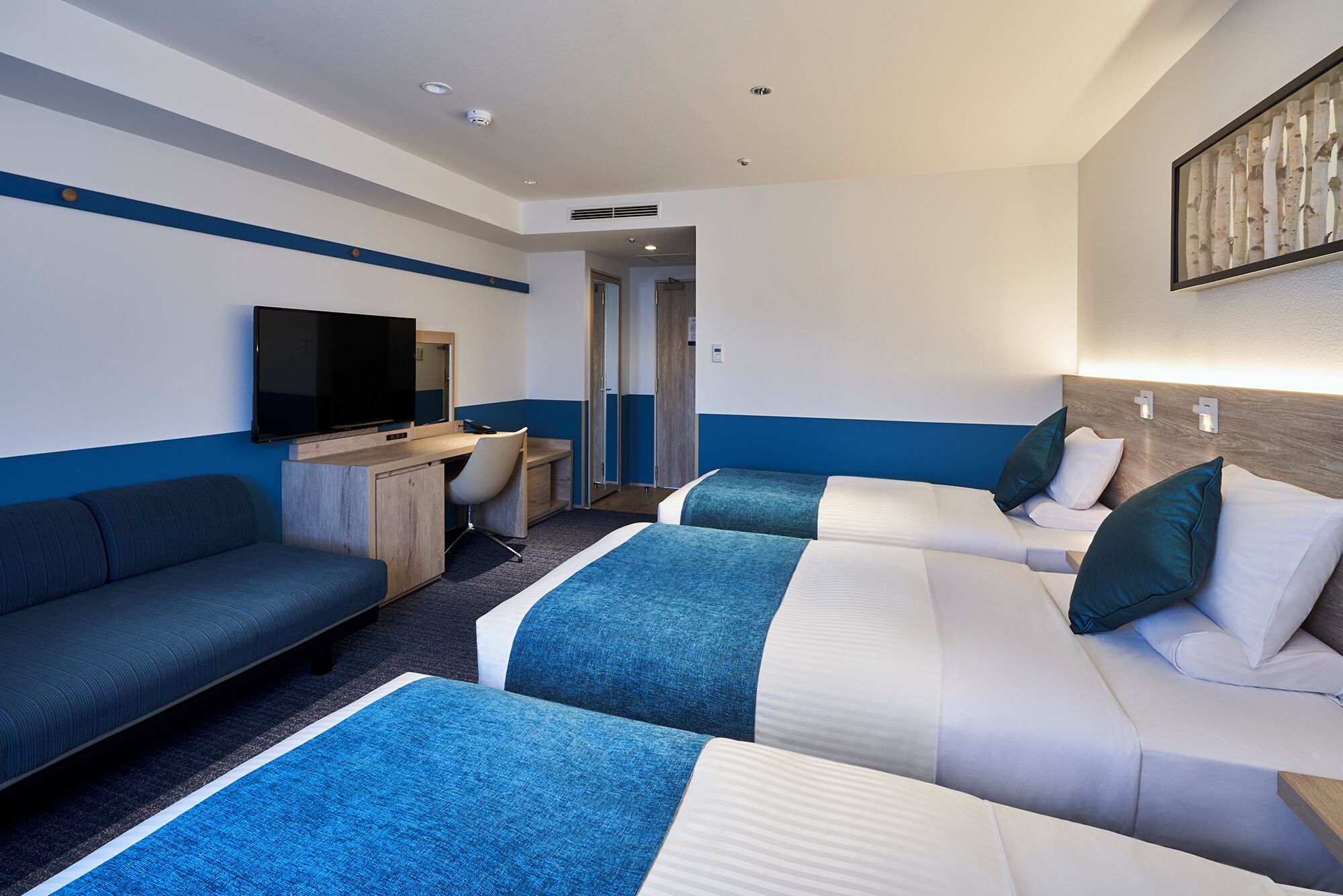 Una habitación de hotel con dos camas, un sofá, un escritorio y un televisor.