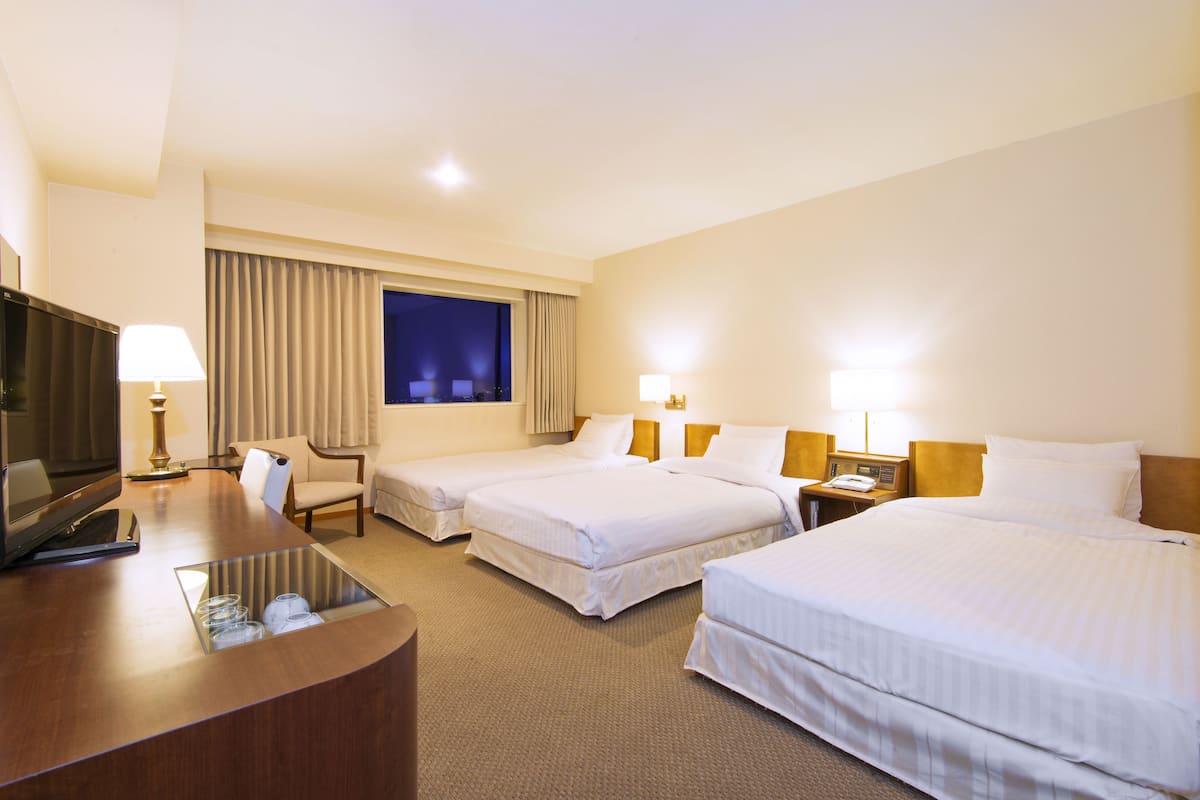 A hotel room with two beds, a desk with a TV, and a large window with curtains.