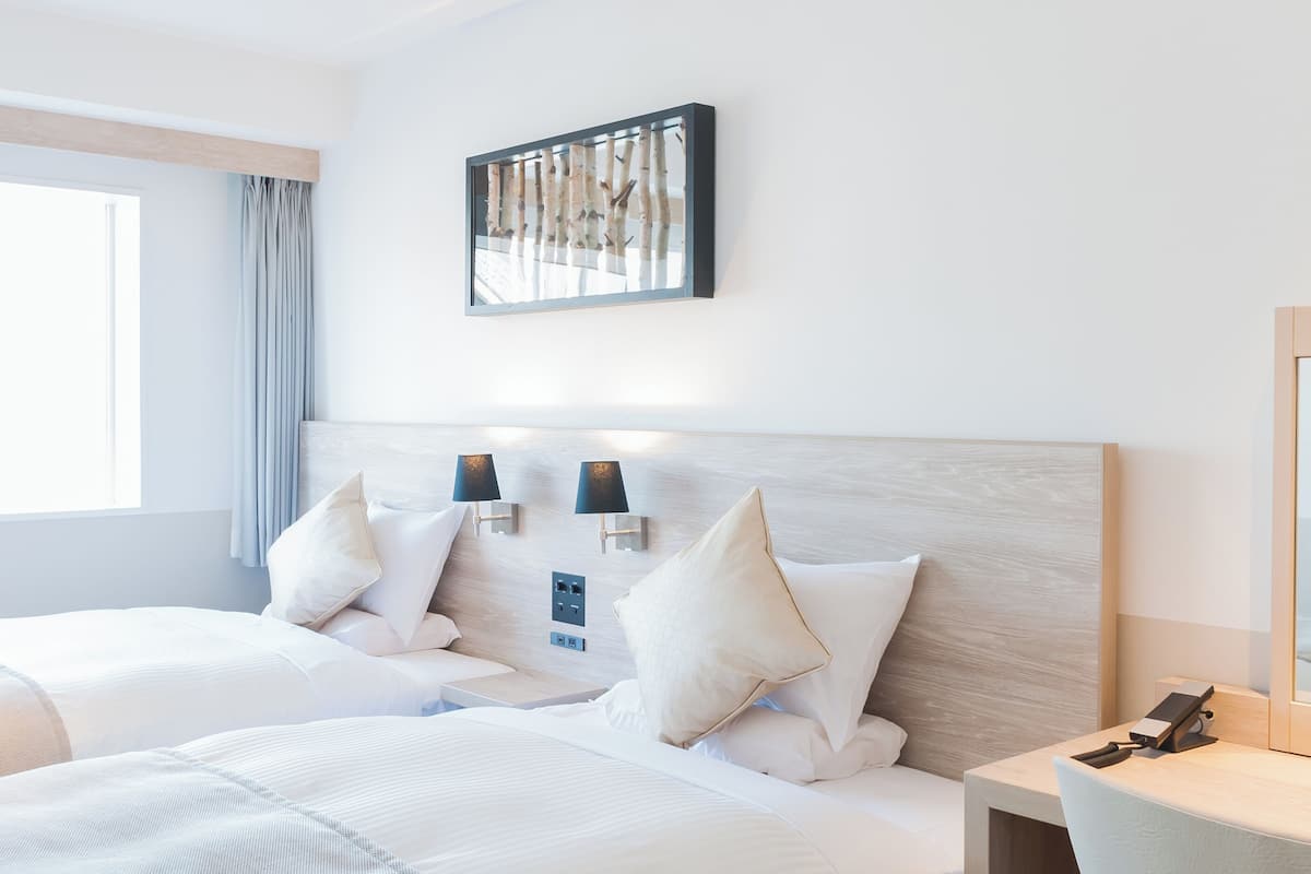 A hotel room with two beds, a large window, and a wall-mounted artwork.