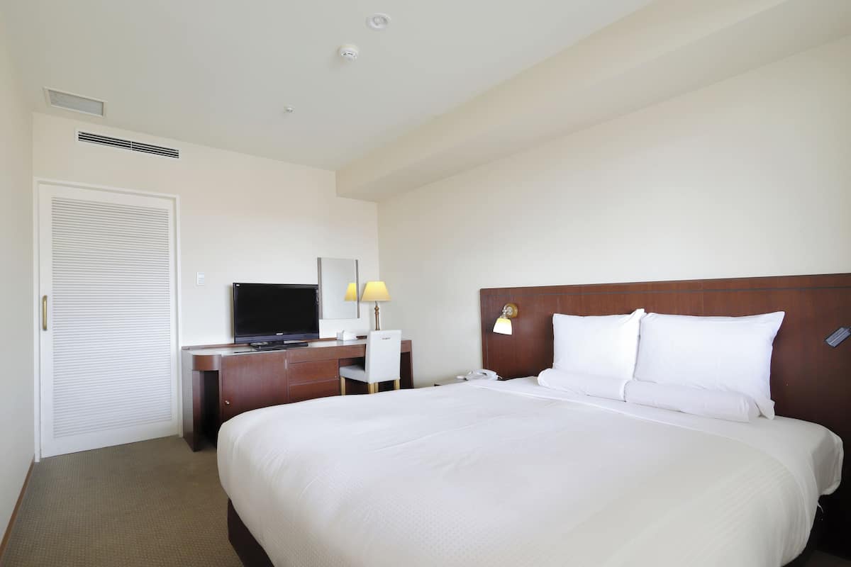 A hotel room with a large bed, a desk with a television, a lamp, and a phone.