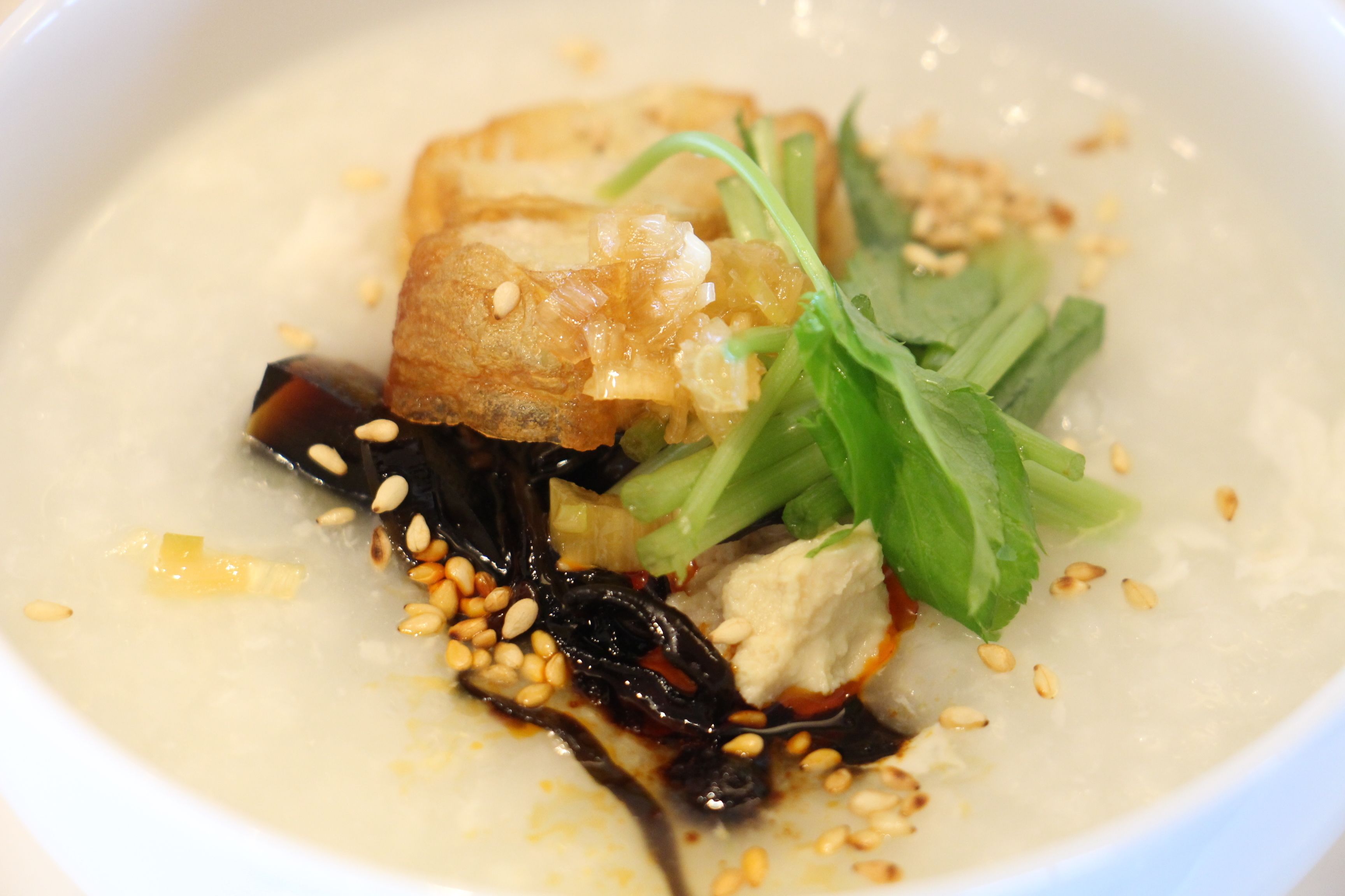 A bowl of soup with tofu, greens, and sesame seeds.