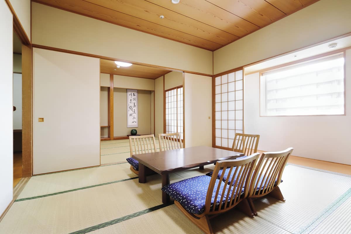 A traditional Japanese room with tatami flooring, a low wooden table, and wooden chairs.