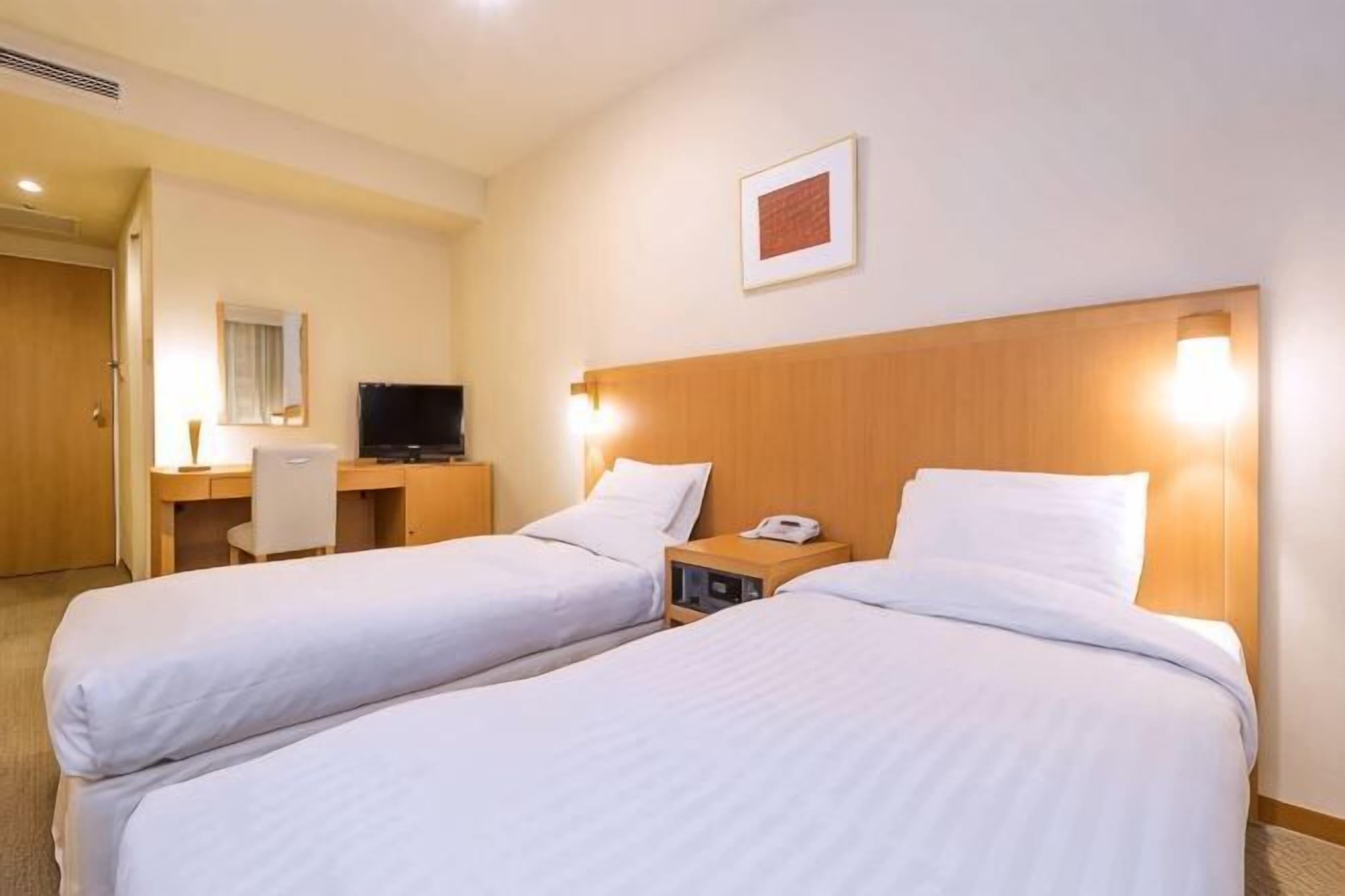 A hotel room with two beds, a desk, a chair, a TV, and a framed picture on the wall.