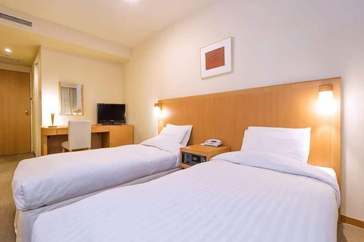 A hotel room with two beds, a desk, a chair, a TV, and a framed picture on the wall.