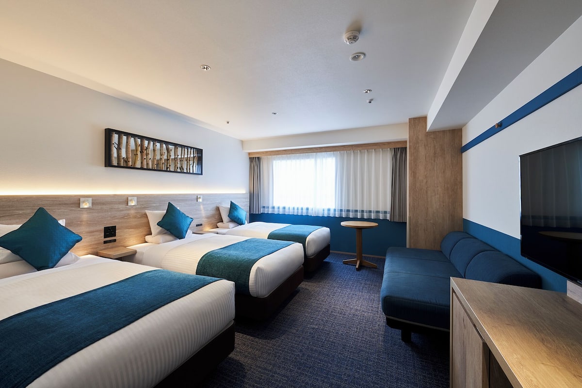 A hotel room with two beds, a sofa, a TV, and a small table.
