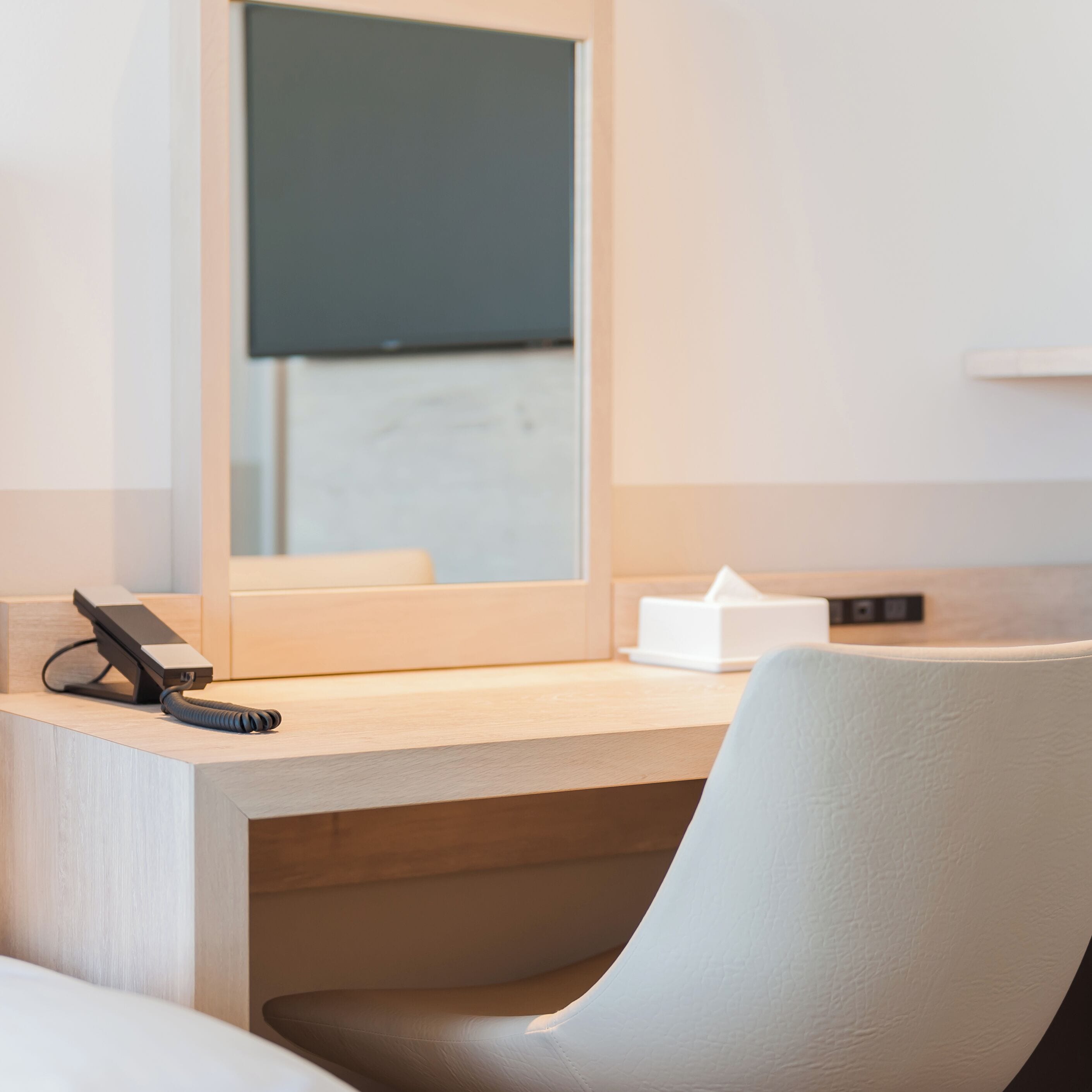 A hotel room with a wooden desk, a chair, a telephone, and a tissue box.