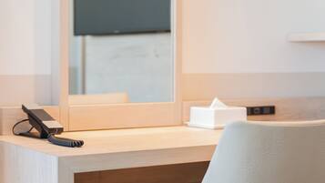 A hotel room with a wooden desk, a chair, a telephone, and a tissue box.