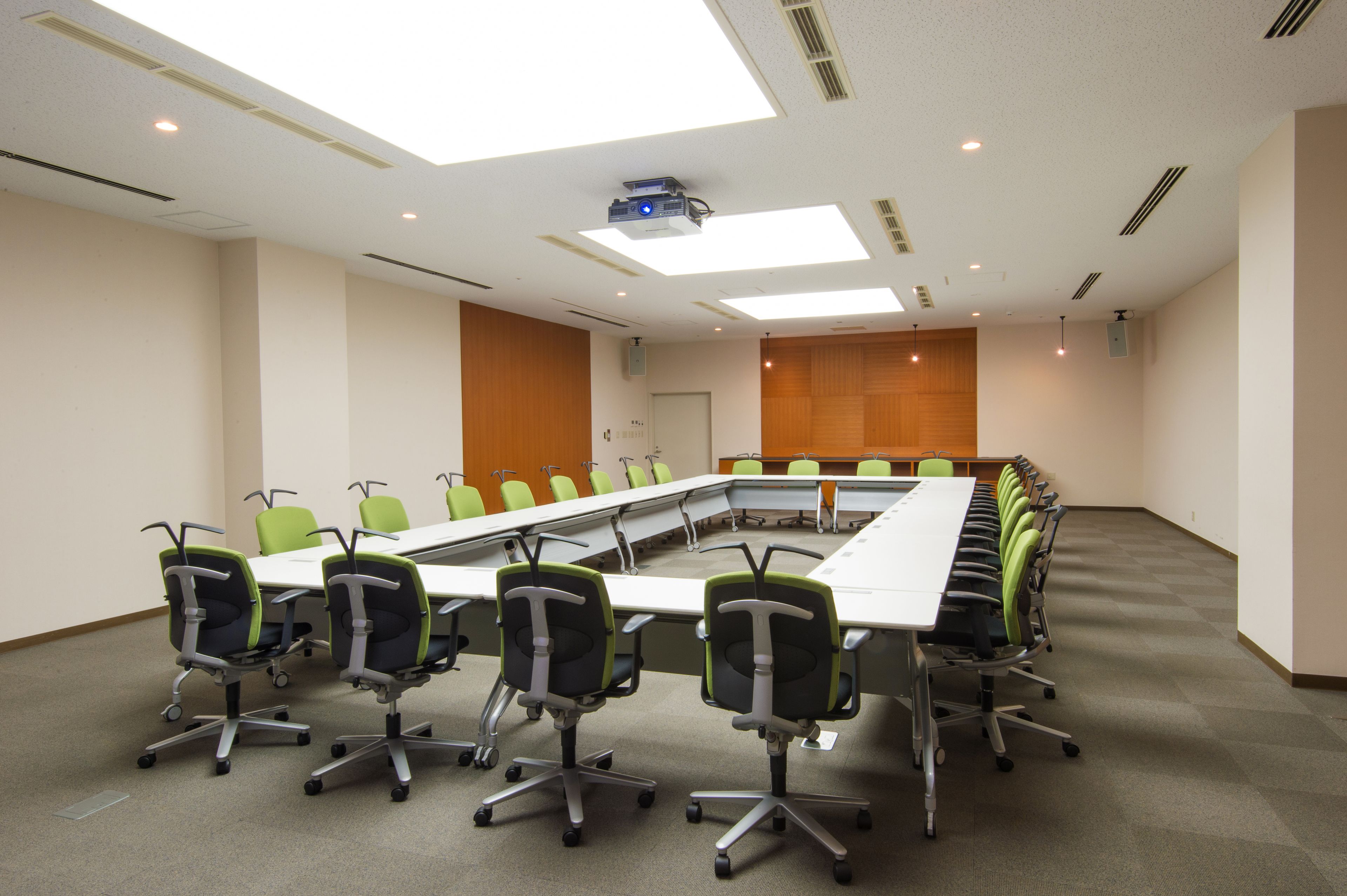A conference room with a long table, green chairs, and a projector.