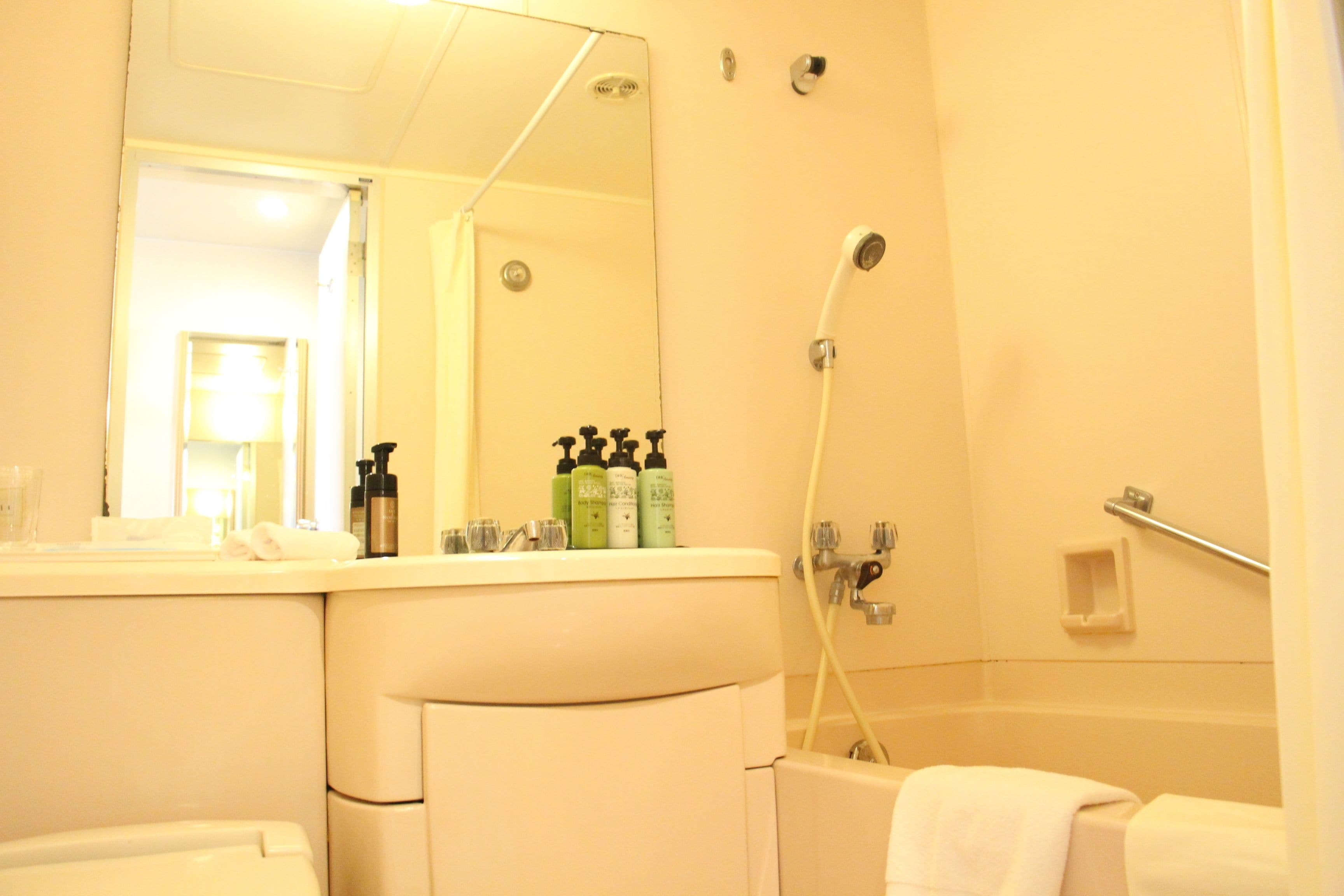 A bathroom with a bathtub, a shower, a sink with toiletries, and a mirror.