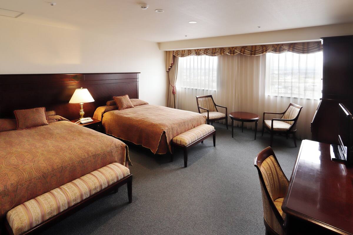 A hotel room with two beds, a desk, a chair, a lamp, and a TV.