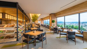 A modern dining area with high tables and chairs, wooden flooring, and large windows offering a city view. - Art Hotel Asahikawa (Asahikawa)