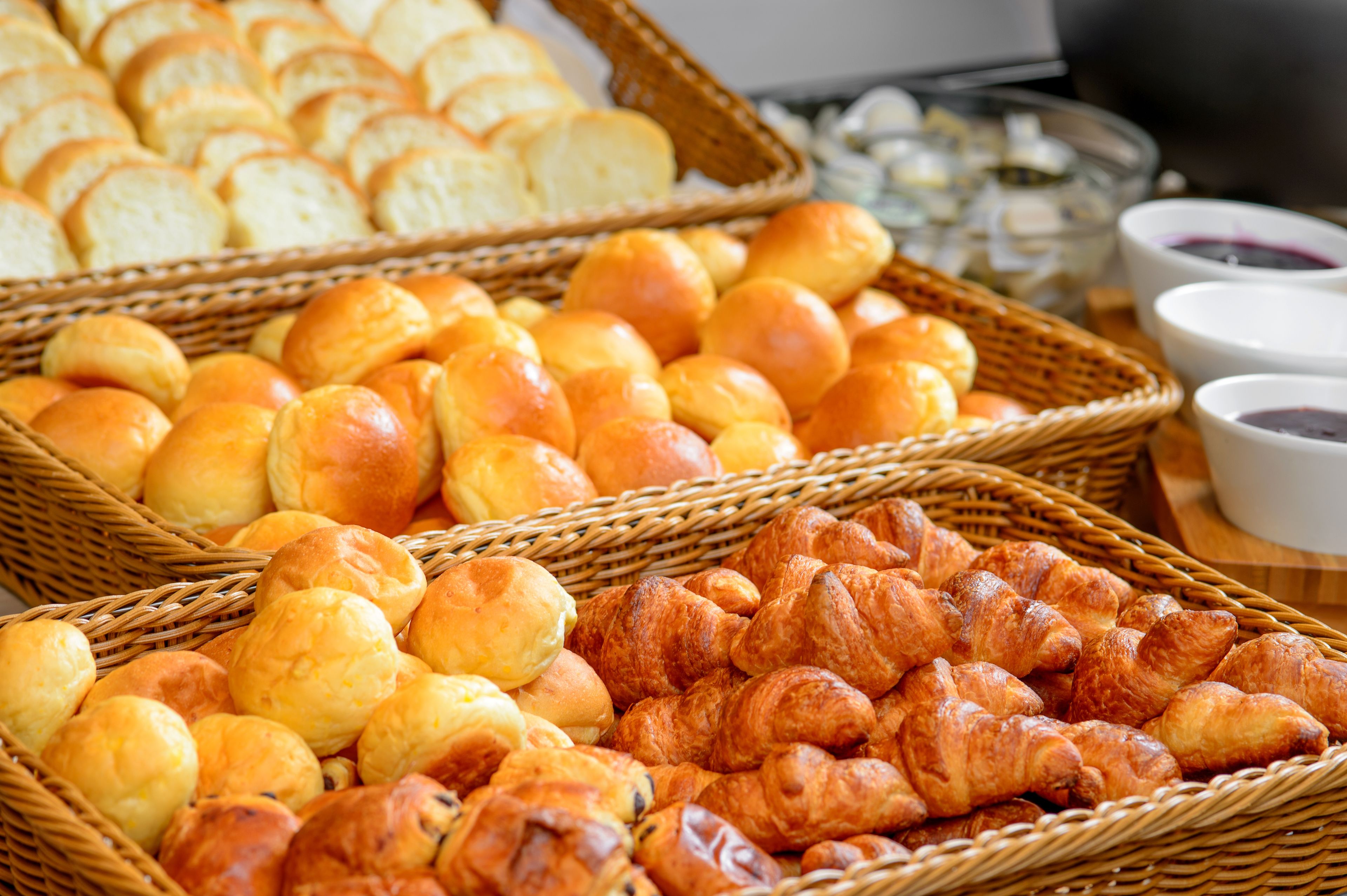 A variety of baked goods including bread rolls and croissants in wicker baskets.