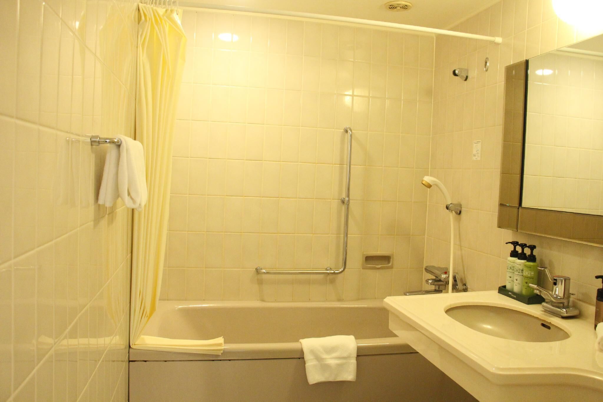 A bathroom with a bathtub, a shower with a grab bar, a sink with soap dispensers, and a mirror.
