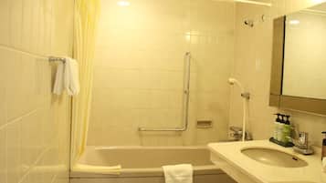 Un baño con bañera, ducha con barra de apoyo, lavamanos con dispensadores de jabón y espejo.