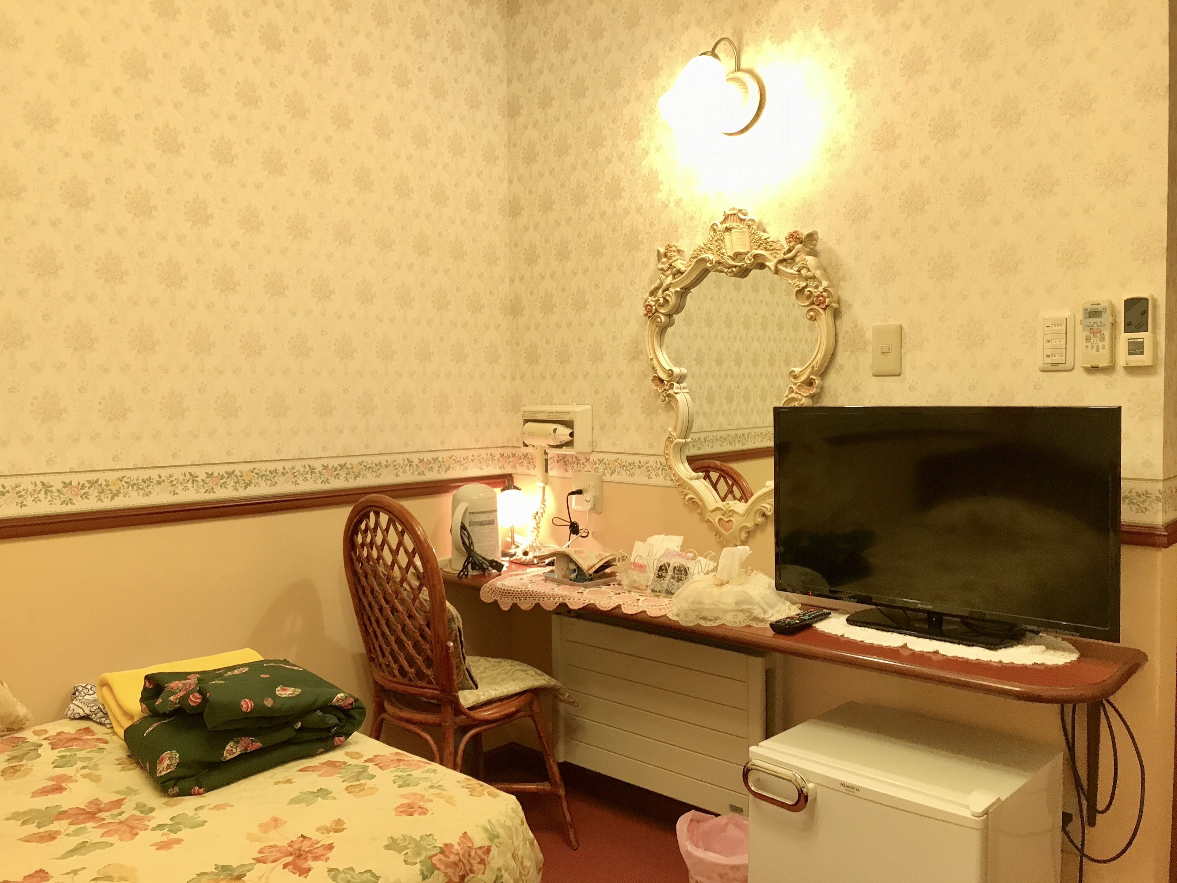 Ein Hotelzimmer mit einem Bett, einem Sessel, einem Schreibtisch mit Fernseher, einem Spiegel und einem kleinen Kühlschrank.