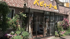 A building with a brick facade, a white picket fence, and a storefront with large yellow signage. - Pension Puppy Tail (Hakodate)