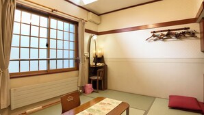 A traditional Japanese room with tatami flooring, a shoji screen, a wooden table, and a futon bed. - Pension Puppy Tail (Hakodate)