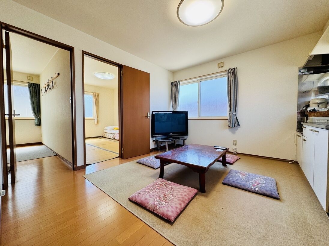 A room with a wooden floor, a television, a table, and a sofa.