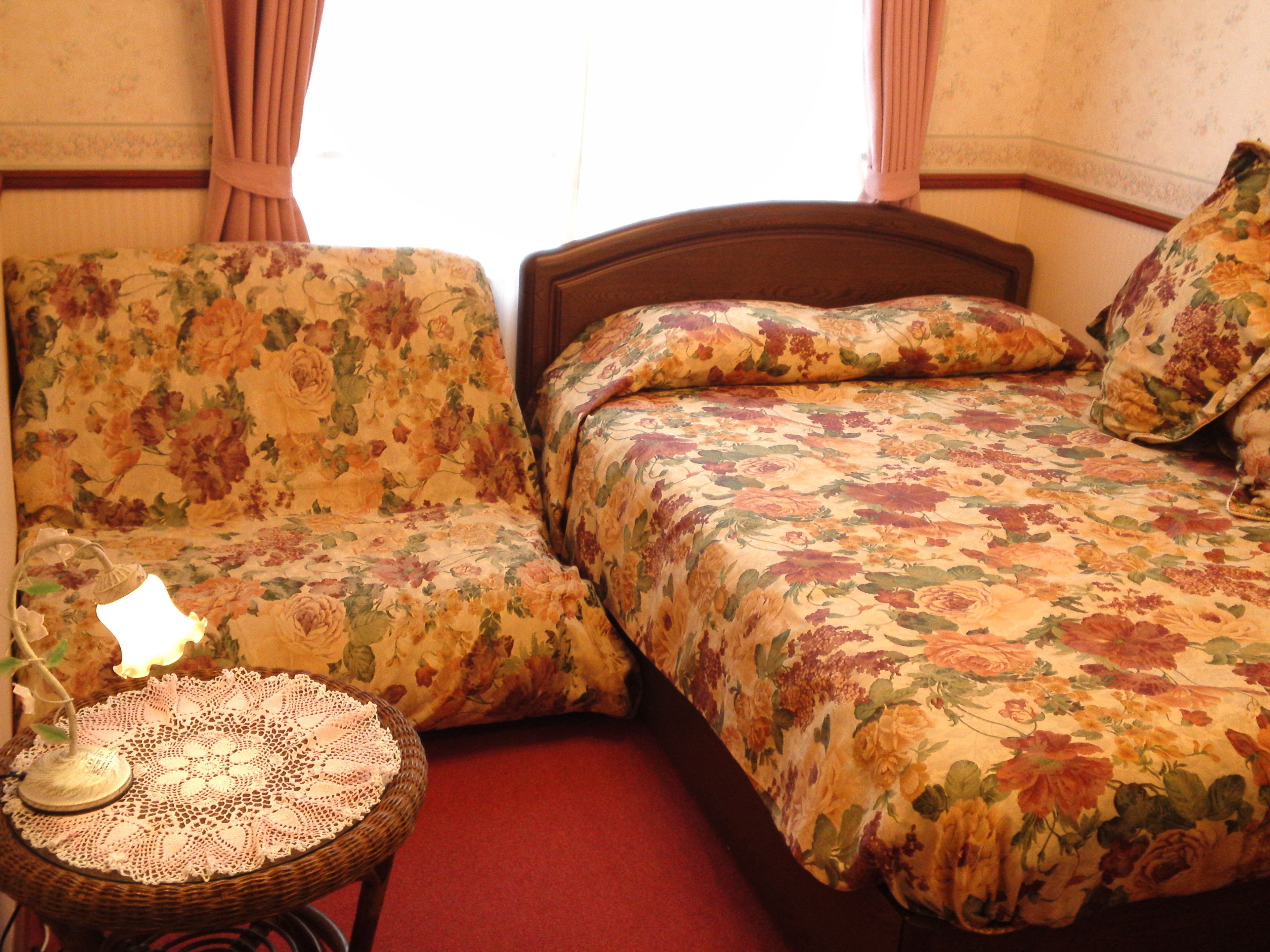 A room with a floral-patterned sofa, a matching bed, and a small table with a doily.