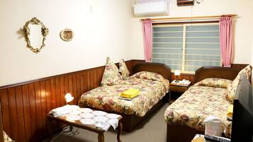 A room with two beds, a table, a TV, and an air conditioning unit.