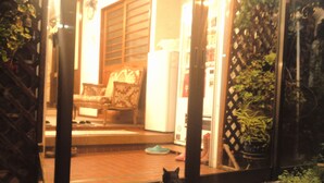 A black cat sitting on a ledge outside a building, looking through a glass door at a room with a chair and a table. - Pension Puppy Tail (Hakodate)