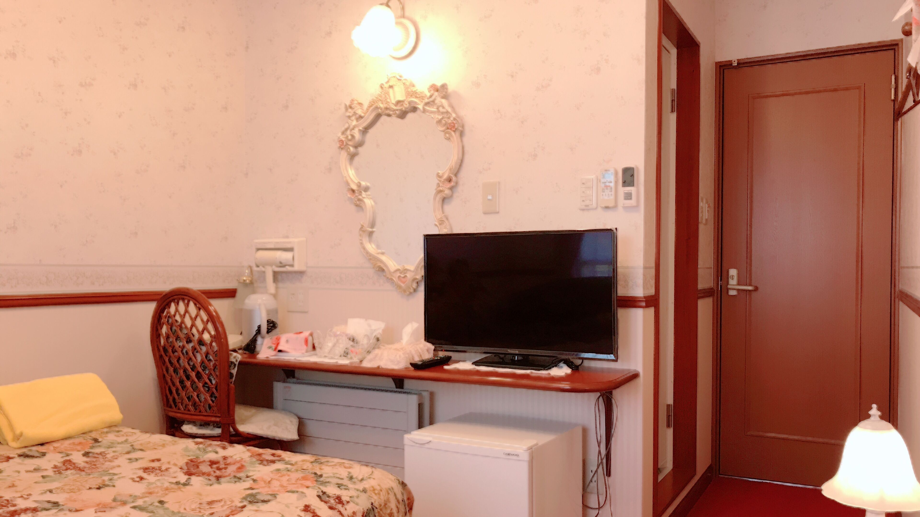 A hotel room with a bed, a desk with a television, a small refrigerator, a chair, and a door.
