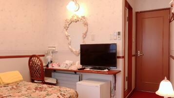 A hotel room with a bed, a desk with a television, a small refrigerator, a chair, and a door.