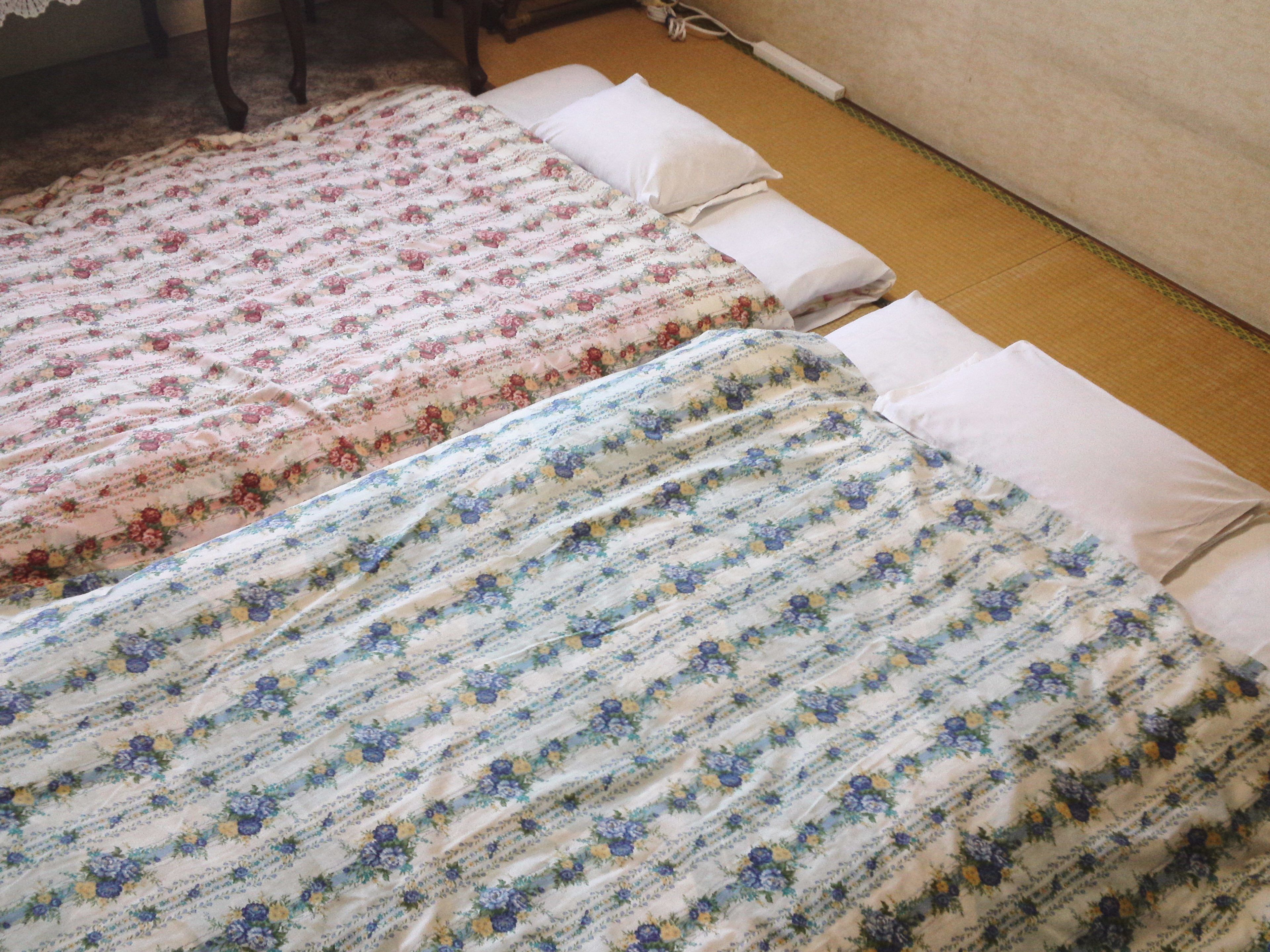 Dos camas con ropa de cama floral, un enchufe y piso de madera.