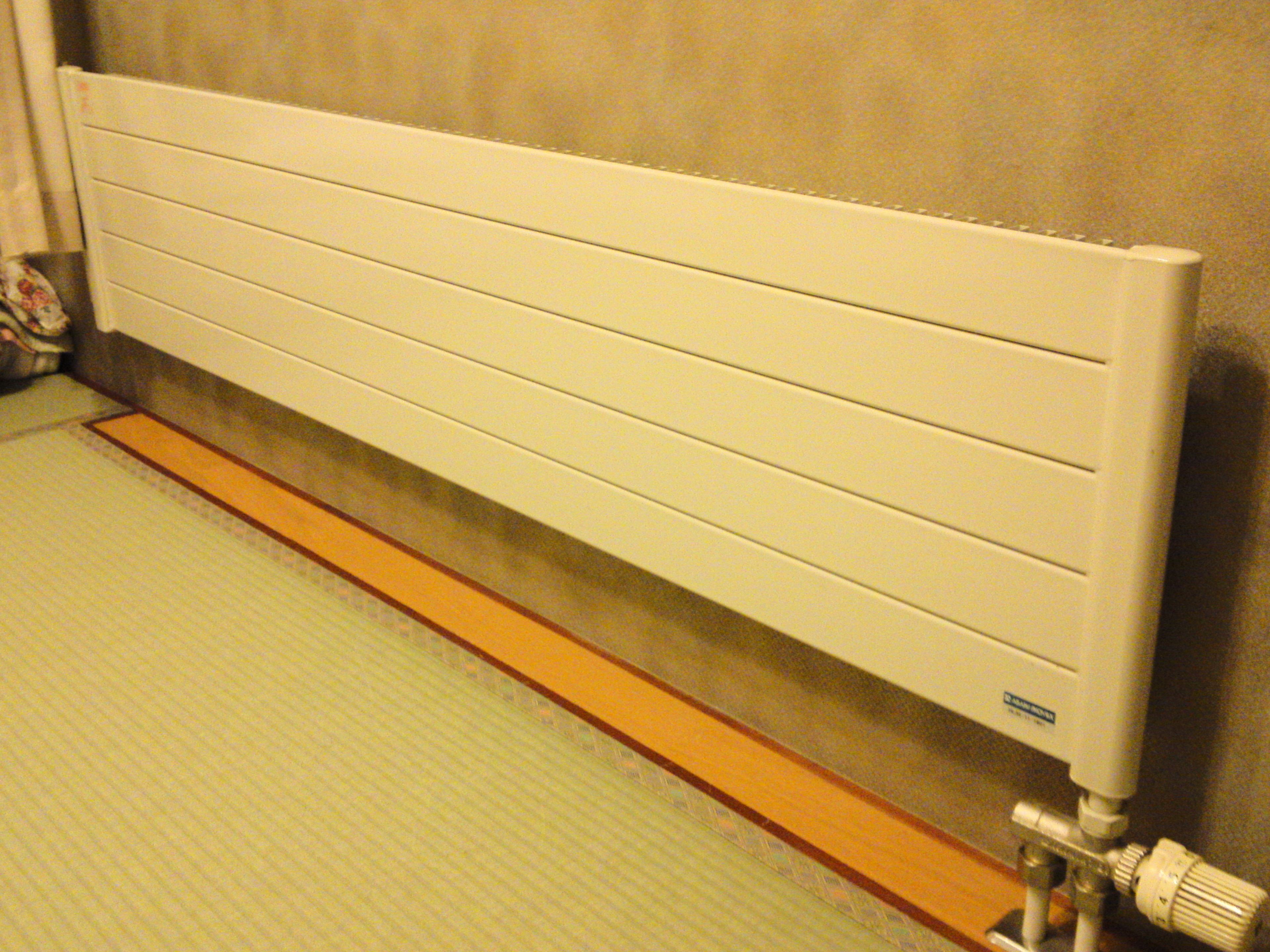 A white radiator with horizontal slats, a wooden base, and a control knob on the right side.