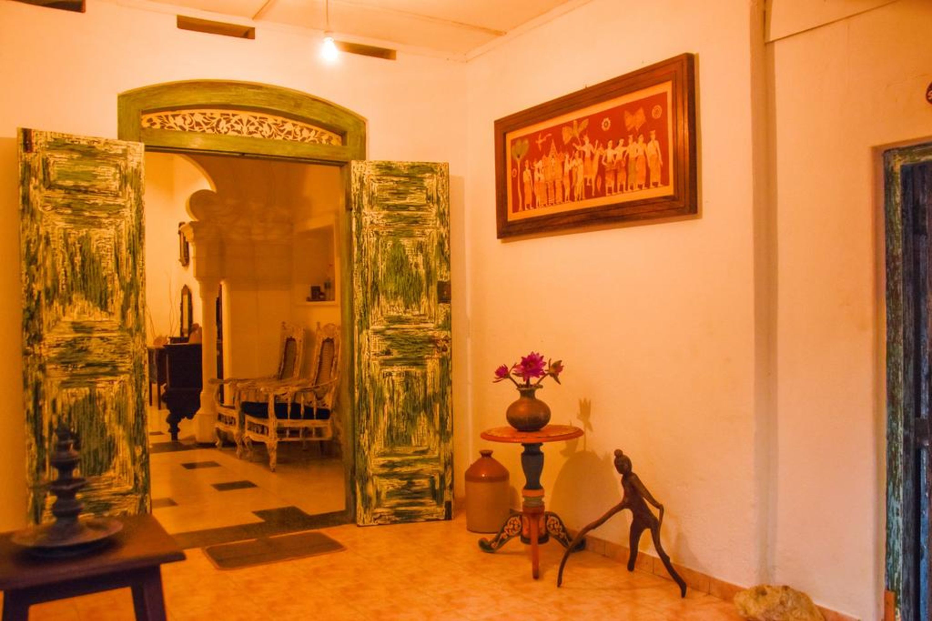 An interior with a wooden door, a framed picture, a vase with flowers, and a small statue.