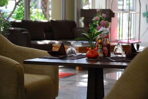 A dining area with a table set for two, a sofa in the background, and a window with a view of greenery. - Summer Spring Hotel (Pattaya)