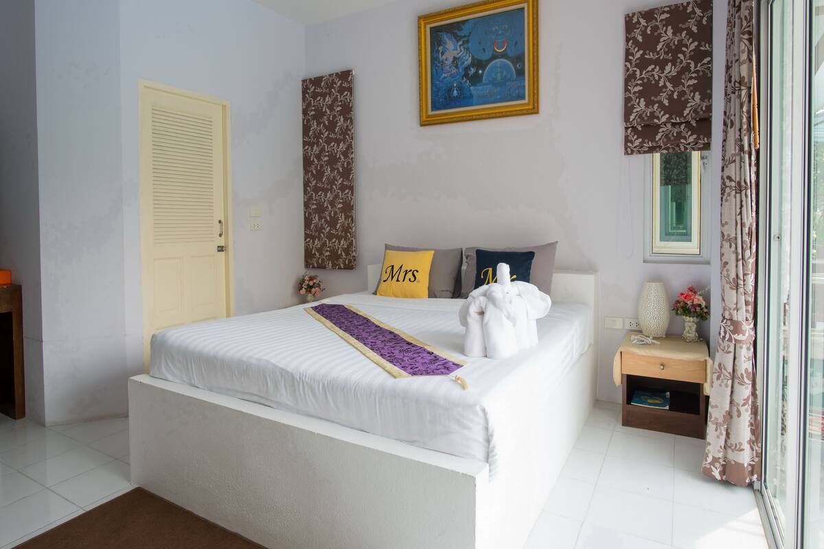 A neatly arranged bedroom with a bed, a bedside table, a nightstand, a window with curtains, and a door.