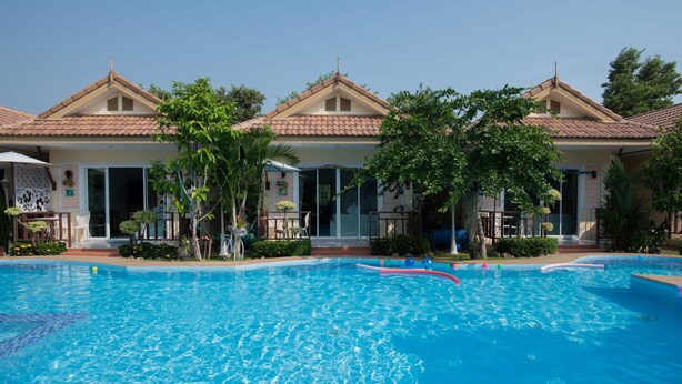 A swimming pool with a clear blue water surface, surrounded by a building with a tiled roof and a covered entrance. - Charm Resort Cha-am (Cha-am)