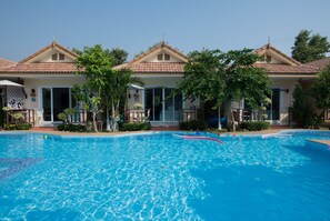 A swimming pool with a clear blue water surface, surrounded by a building with a tiled roof and a covered entrance. - Charm Resort Cha-am (Cha-am)