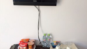 A flat-screen TV mounted on a wall, connected to a device on a table with snacks, drinks, and a remote control. - Charm Resort Cha-am (Cha-am)