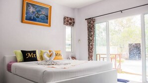 A bedroom with a bed, pillows, a painting, and a view through a sliding door. - Charm Resort Cha-am (Cha-am)