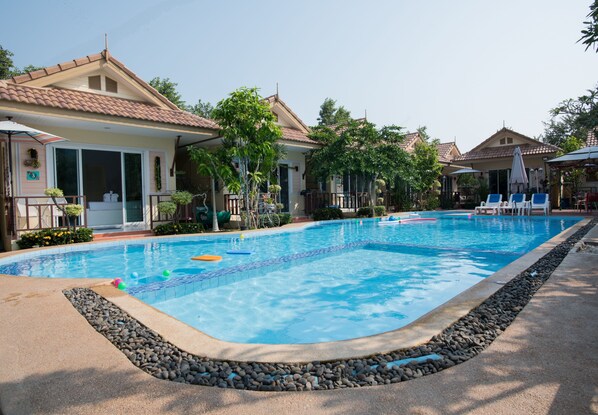 A swimming pool with lounge chairs and umbrellas, surrounded by houses and greenery.